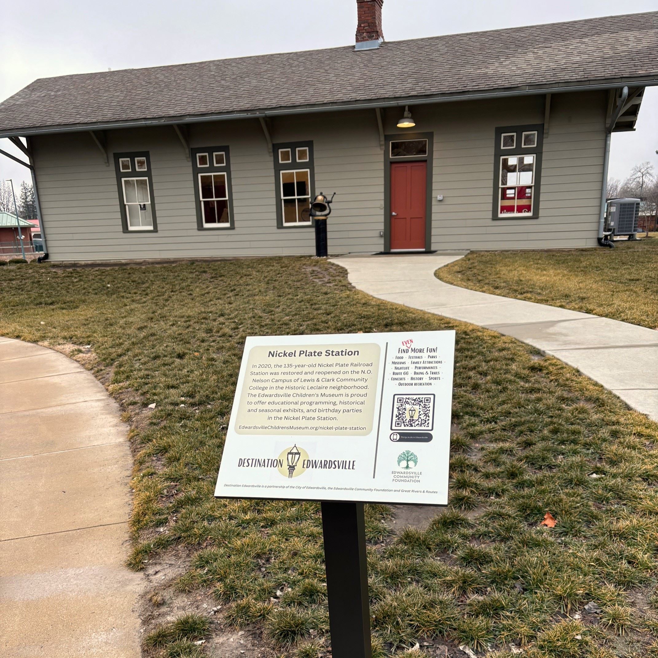 A sign is shown in front of a rectangular building with a red door