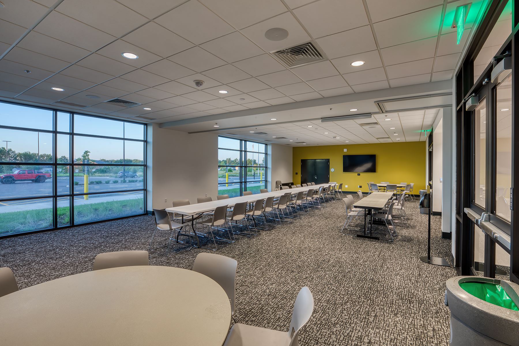 a large room with a yellow wall and windows set up with tables and chairs